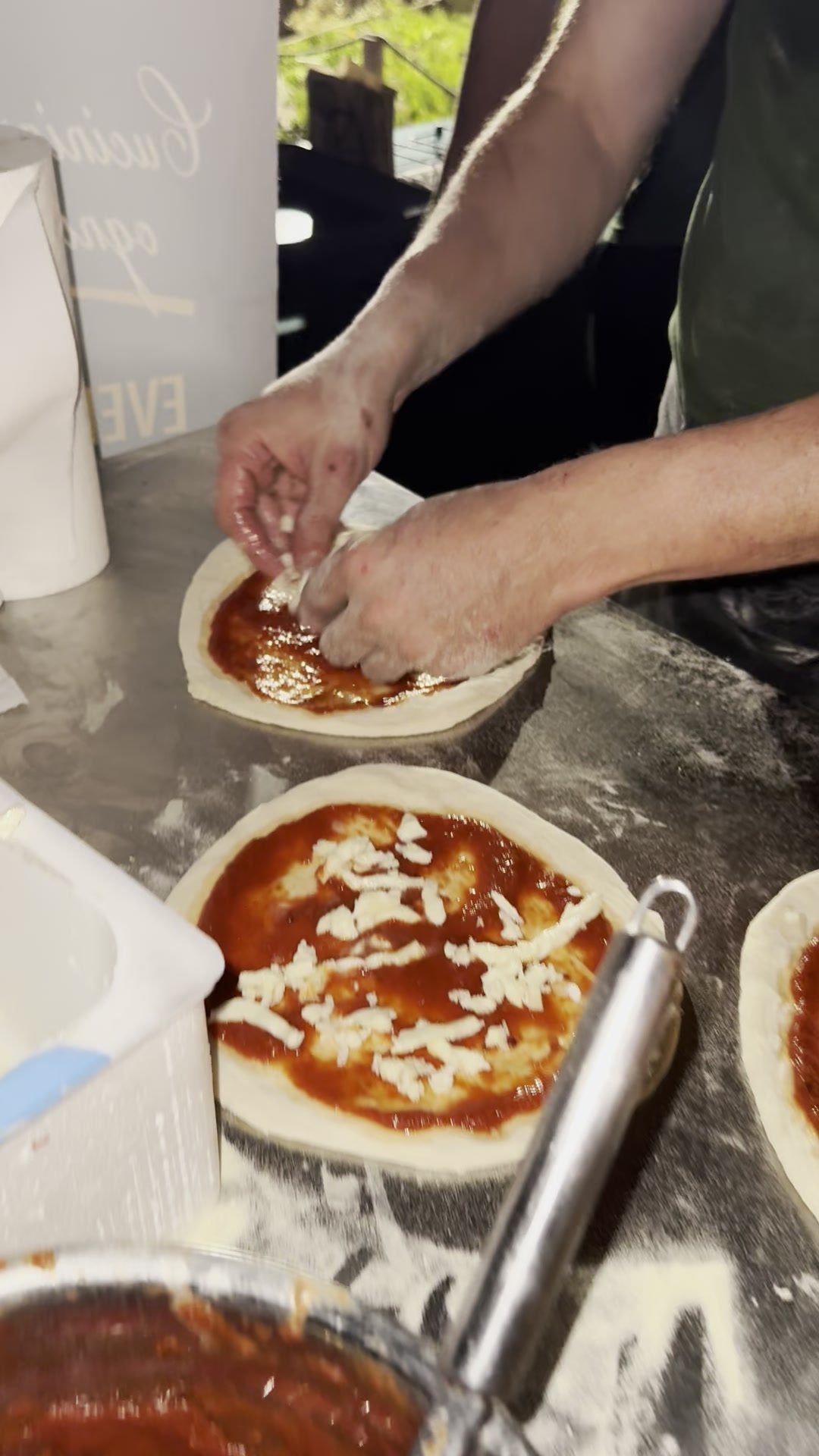Le mani del pizzaiolo condiscono le pizze sul banco infarinato